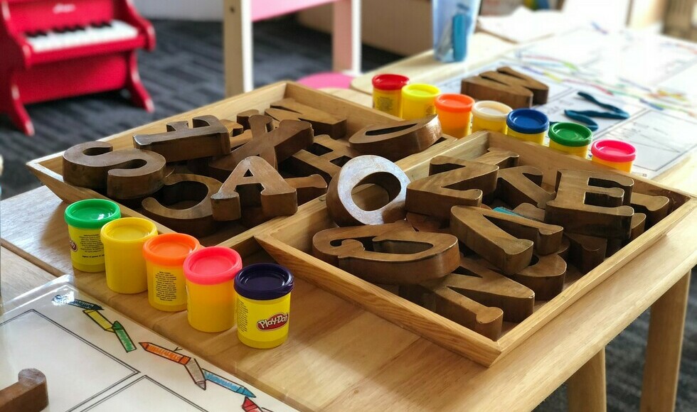 wooden blocks shaped like letters and containers of modelling clay on a table